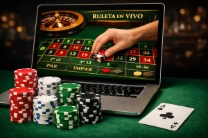 Laptop con ruleta online, fichas de casino apiladas y mano apostando en la mesa verde